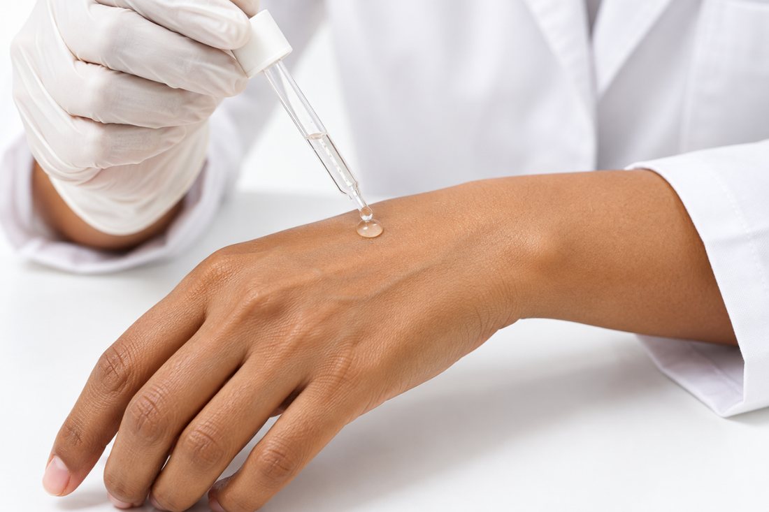 Gloved hand applying a drop of clear skincare serum to the back of a hand